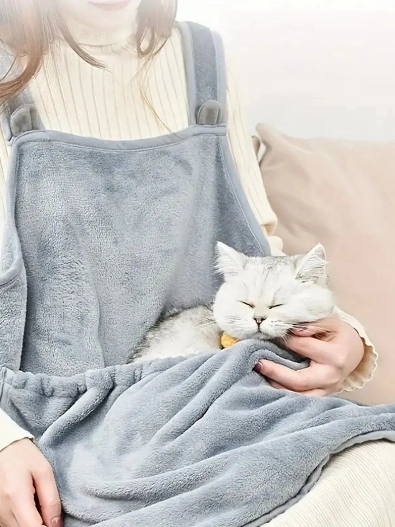 Person holding a cat wrapped in a gray blanket with a neutral background